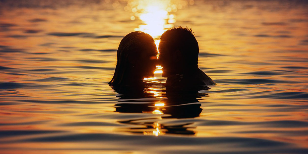 sesso sotto alla riva della spiaggia, sotto l'acqua, all'alba